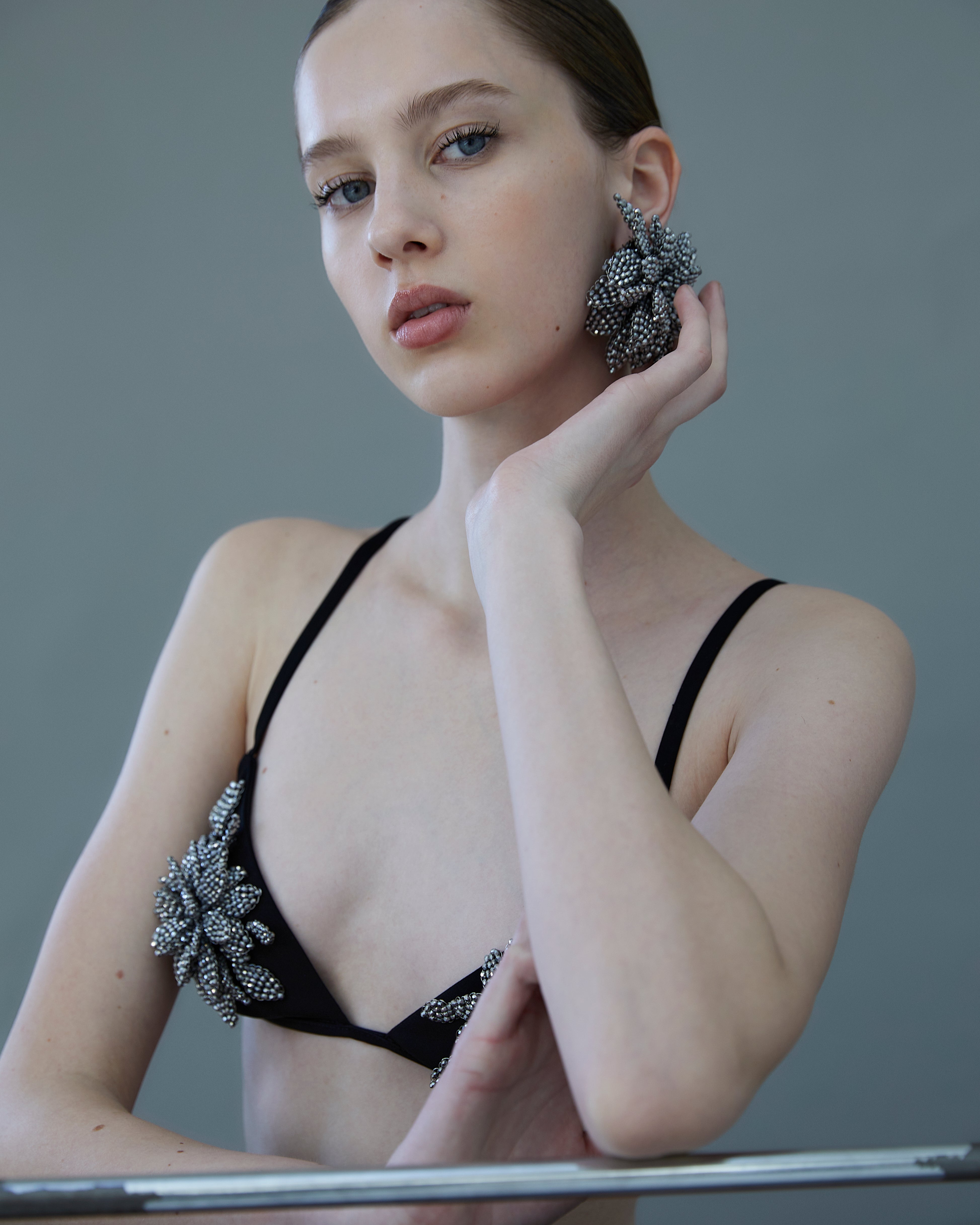 emale model wearing black crepe bra with crystal embroidery styled with high-waist black trousers.